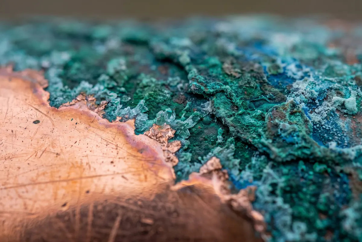 A sheet of copper caught mid-transition, bare penny-bright metal giving way along a ragged frontier to dense blue-green patina.