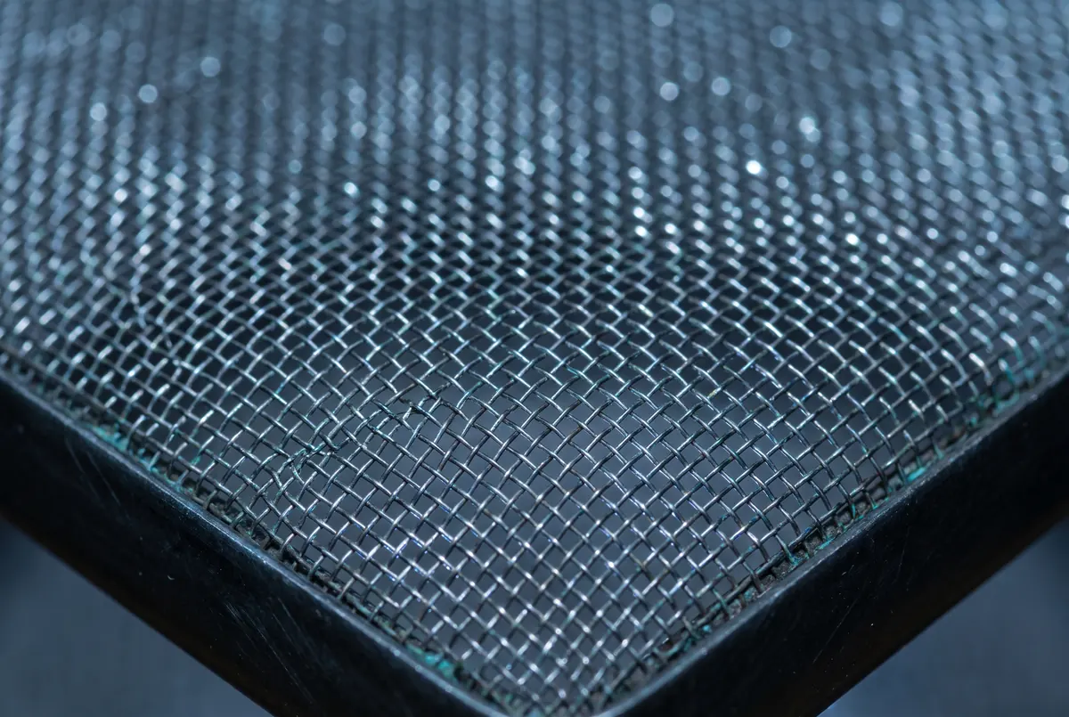 Fine stainless micro-mesh stretched over a frame, backlit so the weave reads as a field of tiny bright apertures.