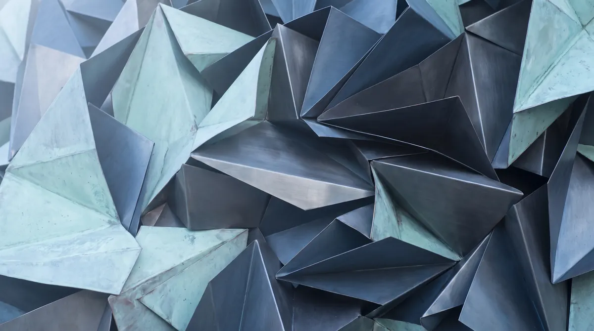 Many sheets of formed metal in cool grays and faint green, folded at crisp angles and layered over one another into a faceted field.