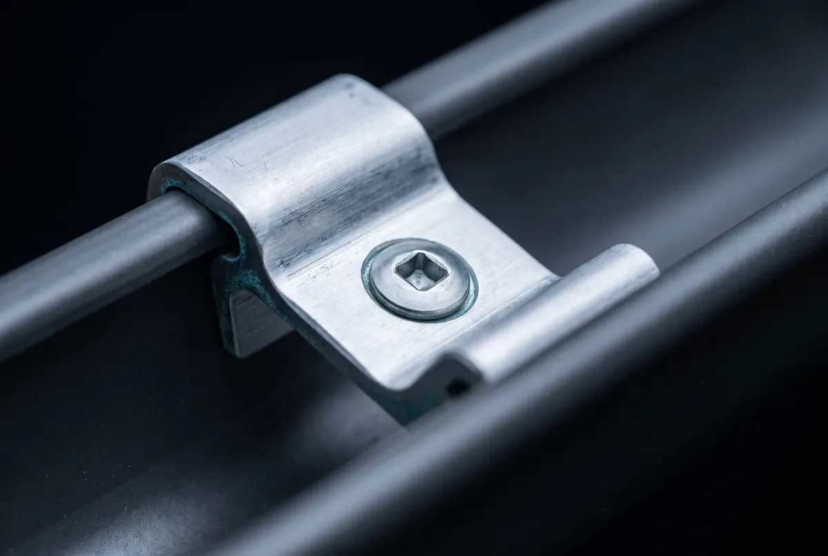 A metal hanger bracket clipped inside a gutter channel, its screw seated square, lit hard from one side.