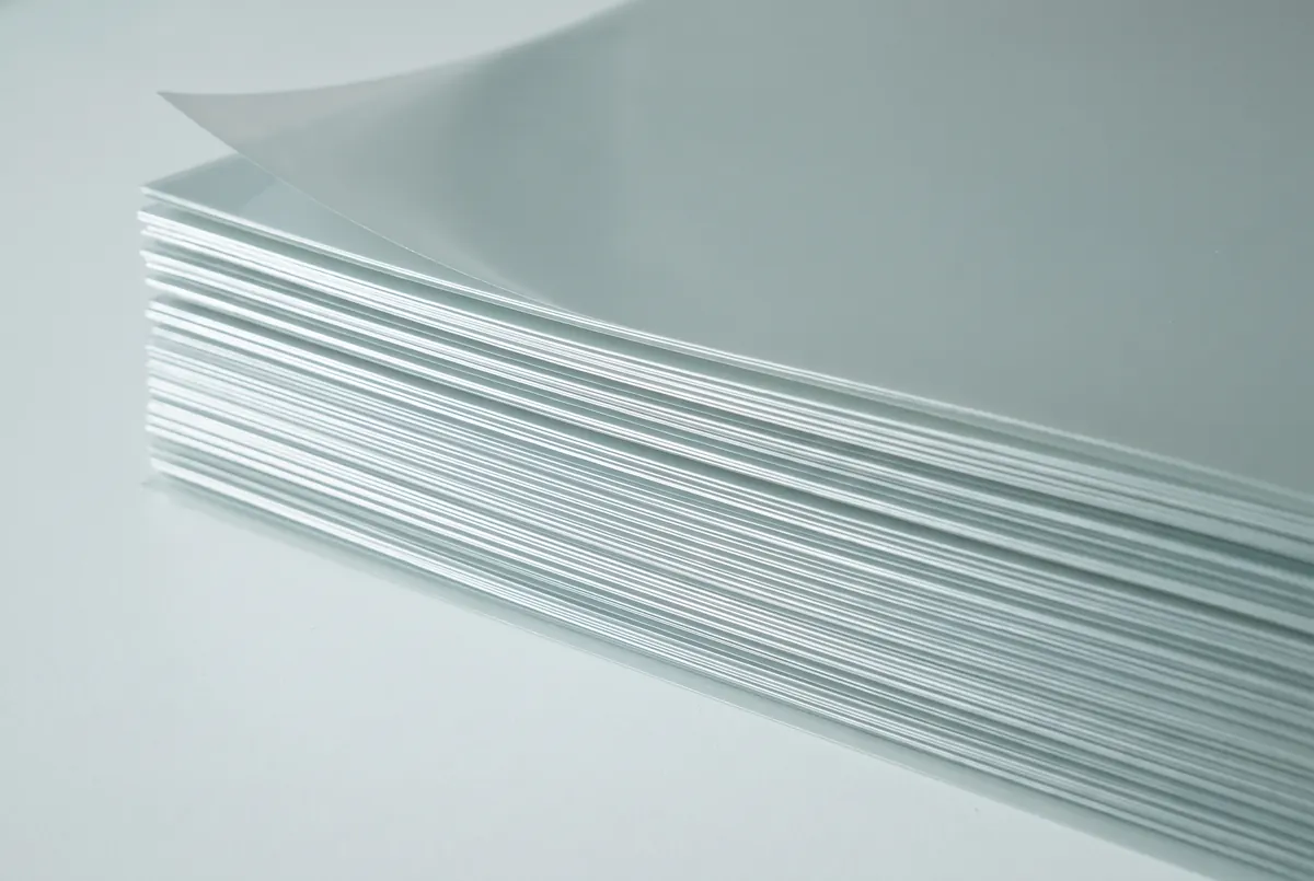 A stack of blank pale drafting film seen at a raking angle, the layered edges building a striped horizon of fine bright lines.