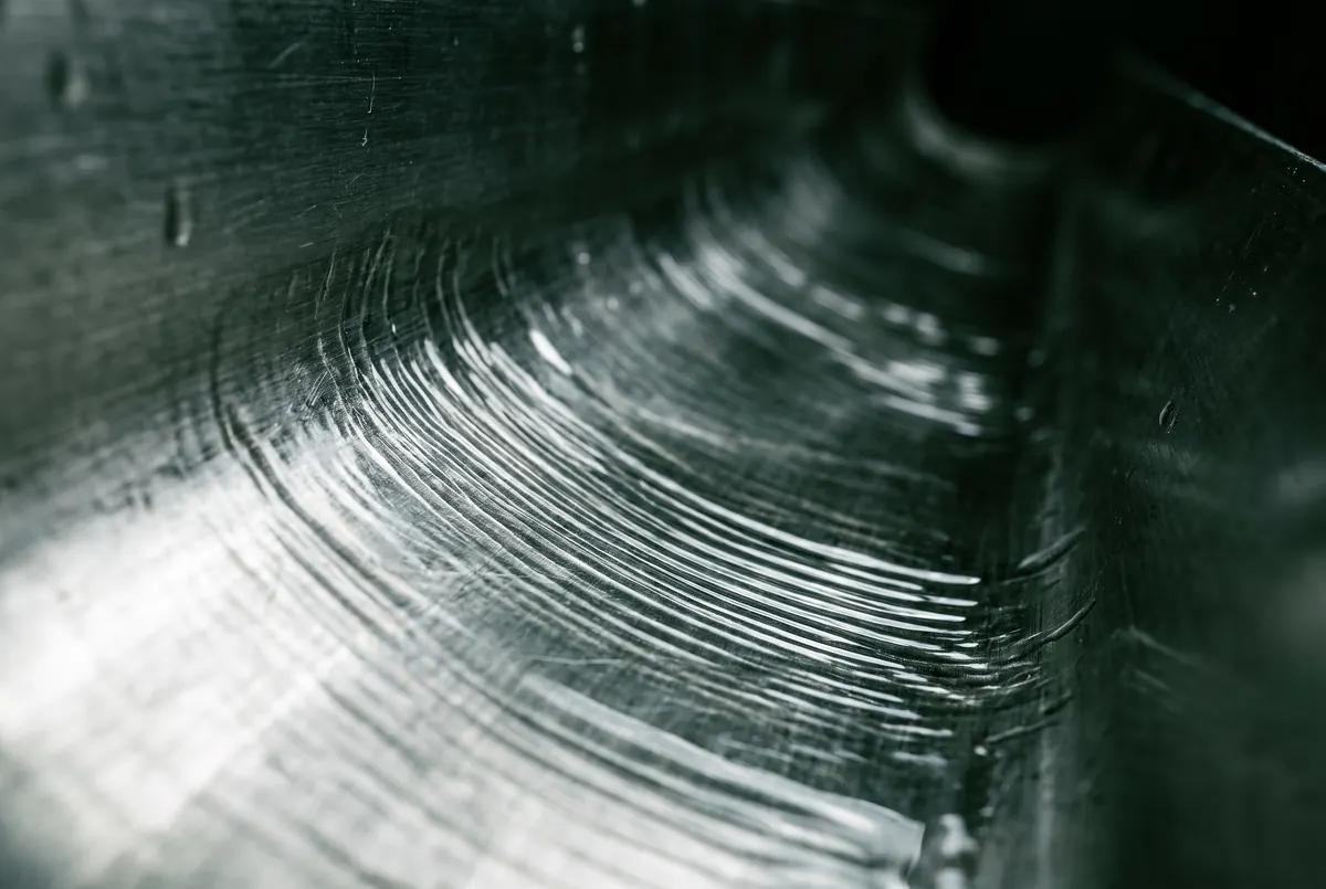 A thin film of water running along the inside of a metal channel, its surface breaking into fine parallel ripples that show the direction of flow.
