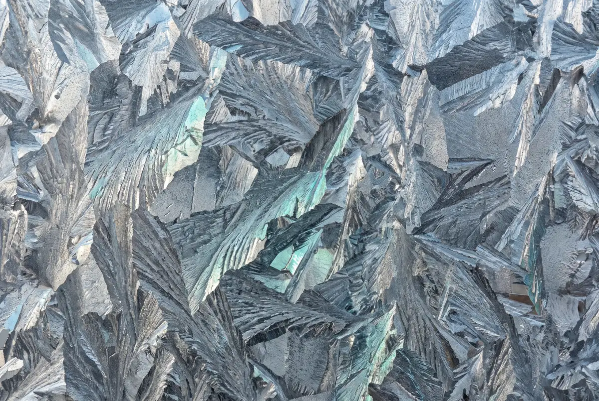 The crystalline spangle pattern of a hot-dip galvanized zinc coating, large feathery crystals catching light at different angles.
